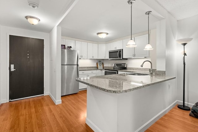 kitchen featuring light wood finished floors, a peninsula, appliances with stainless steel finishes, and a sink