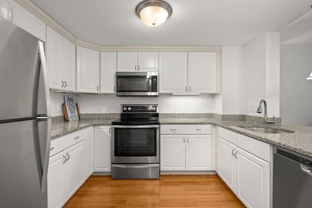 kitchen featuring light stone counters, stainless steel appliances, light wood-style floors, white cabinetry, and a sink