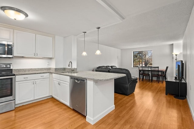 kitchen with a peninsula, appliances with stainless steel finishes, a sink, and light wood-style flooring