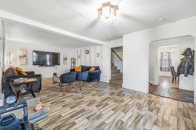 living room with stairway, wood finished floors, arched walkways, a notable chandelier, and a textured ceiling