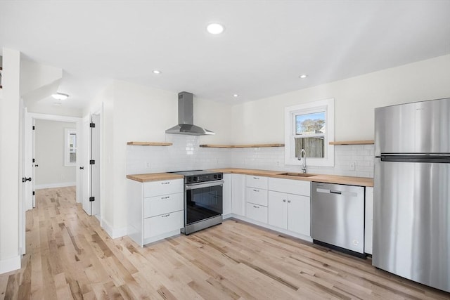 kitchen featuring butcher block counters, sink, wall chimney range hood, white cabinets, and appliances with stainless steel finishes