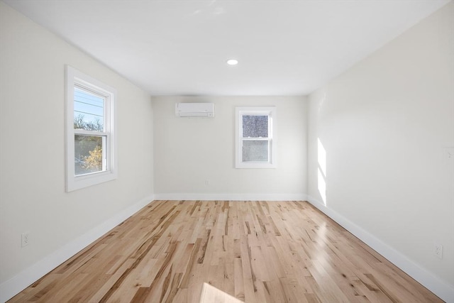 unfurnished room with a wall unit AC and light hardwood / wood-style flooring