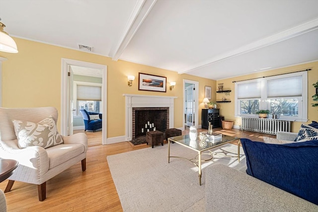 living room featuring a brick fireplace, beam ceiling, radiator heating unit, and light hardwood / wood-style floors