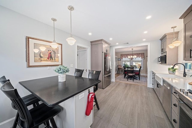 kitchen with gray cabinets, high quality fridge, pendant lighting, a breakfast bar area, and light hardwood / wood-style flooring