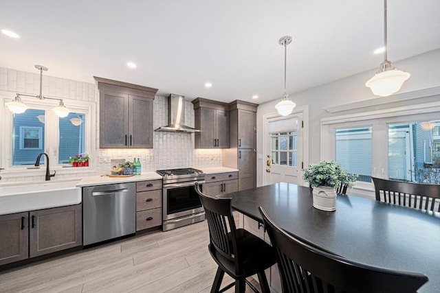 kitchen with sink, decorative light fixtures, stainless steel appliances, and wall chimney exhaust hood