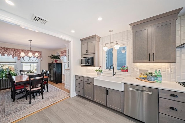 kitchen featuring appliances with stainless steel finishes, pendant lighting, sink, a notable chandelier, and light hardwood / wood-style floors