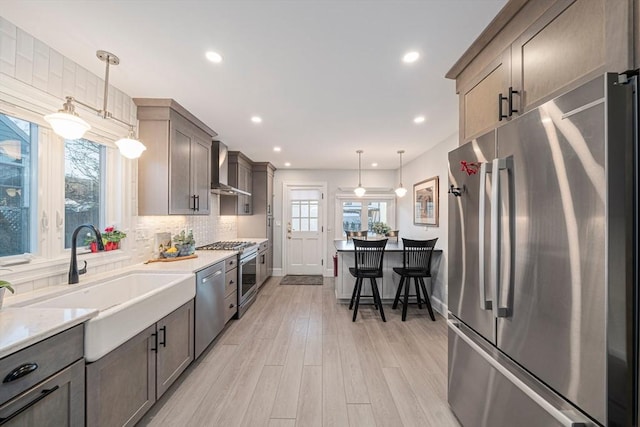 kitchen featuring pendant lighting, wall chimney range hood, sink, appliances with stainless steel finishes, and backsplash