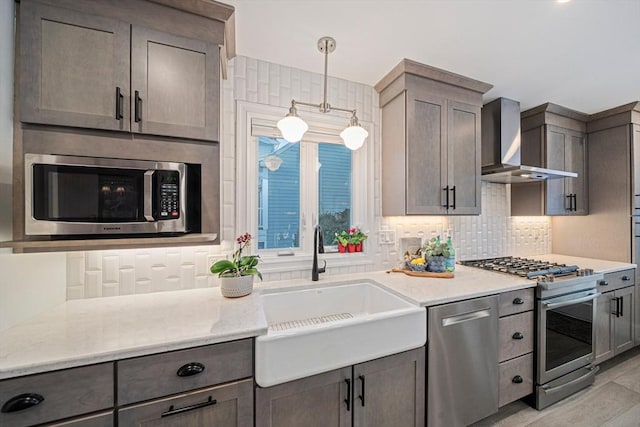 kitchen with sink, light hardwood / wood-style flooring, appliances with stainless steel finishes, pendant lighting, and wall chimney range hood