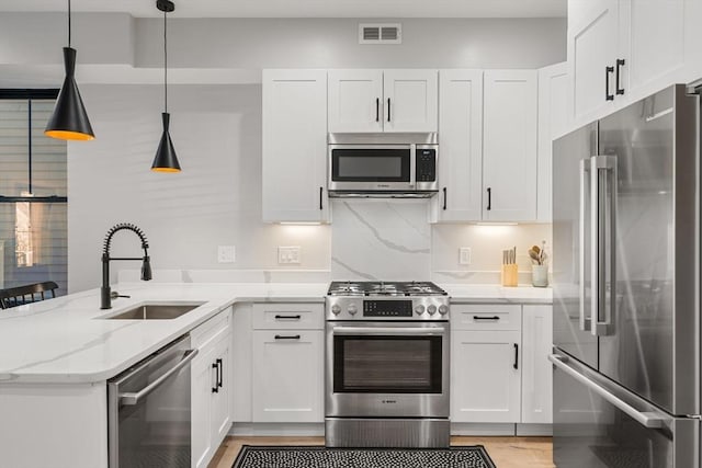 kitchen featuring pendant lighting, stainless steel appliances, light stone counters, and white cabinets