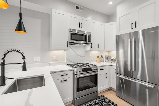 kitchen featuring pendant lighting, sink, appliances with stainless steel finishes, white cabinetry, and light stone counters