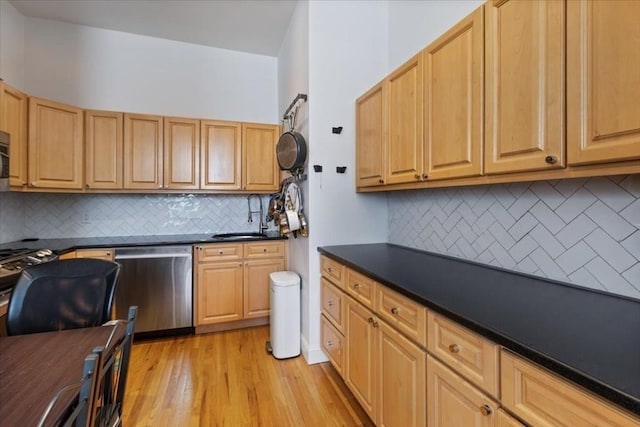 kitchen with dishwasher, backsplash, dark countertops, a sink, and light wood finished floors