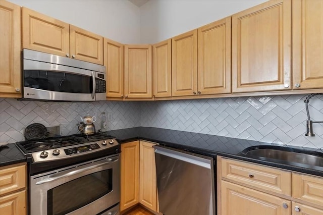 kitchen with stainless steel appliances, dark countertops, light brown cabinetry, a sink, and decorative backsplash