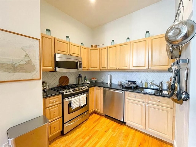 kitchen featuring appliances with stainless steel finishes, a sink, dark countertops, light wood finished floors, and backsplash