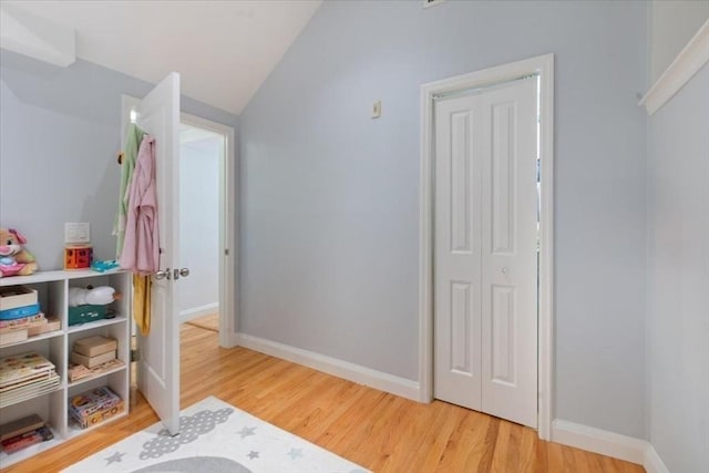bedroom with light wood-style flooring, vaulted ceiling, and baseboards