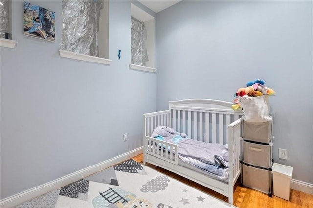 bedroom with a crib, wood finished floors, and baseboards