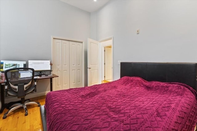 bedroom with wood finished floors, a towering ceiling, a desk, and a closet