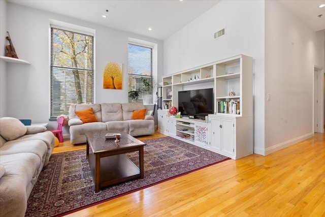 living room with wood finished floors, recessed lighting, a towering ceiling, and baseboards