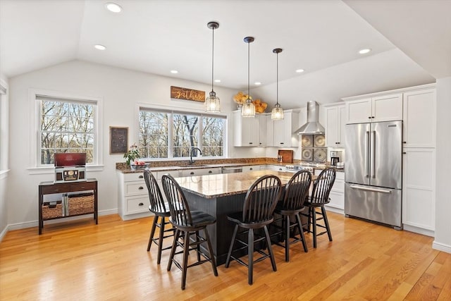 kitchen featuring a center island, decorative light fixtures, wall chimney range hood, stainless steel appliances, and white cabinets