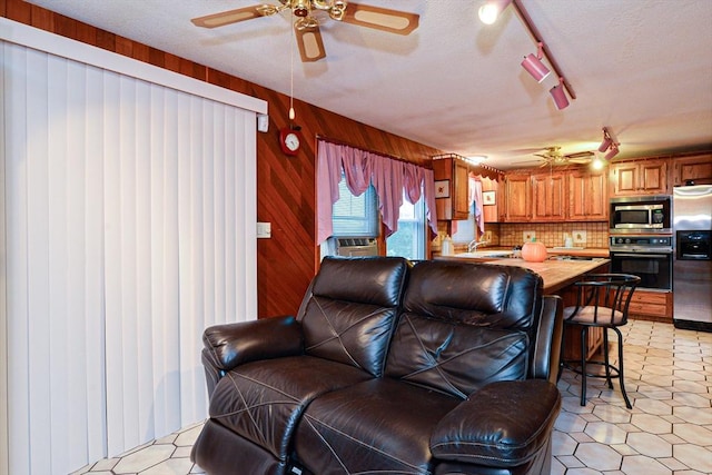 living area with ceiling fan, track lighting, and wooden walls
