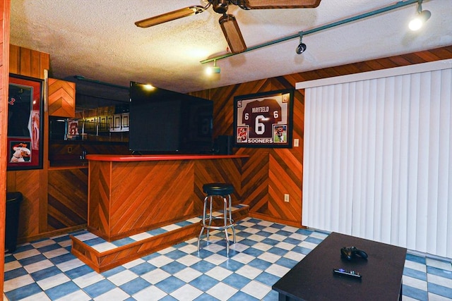 indoor wet bar featuring tile patterned floors, ceiling fan, wood walls, track lighting, and a textured ceiling