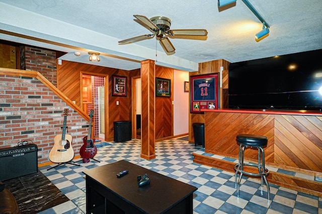 living area with tile patterned floors, wooden walls, a ceiling fan, a textured ceiling, and a bar