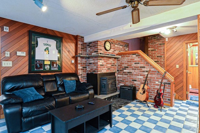 living room featuring wooden walls, tile patterned floors, ceiling fan, a wood stove, and a textured ceiling