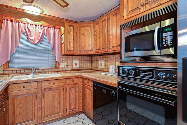 kitchen with black appliances, a sink, backsplash, brown cabinetry, and a textured ceiling