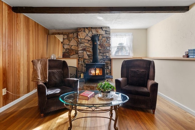 living area with beam ceiling, wood-type flooring, a wood stove, and wooden walls