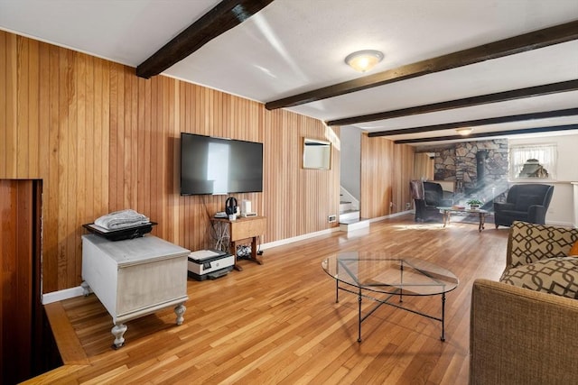 living room featuring beamed ceiling, light hardwood / wood-style floors, a wood stove, and wooden walls