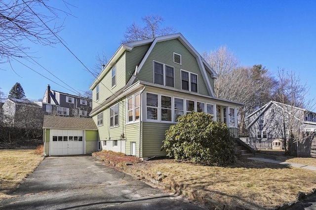 view of front facade featuring aphalt driveway, a gambrel roof, an outbuilding, and a garage