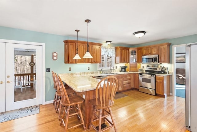 kitchen with appliances with stainless steel finishes, hanging light fixtures, light wood-type flooring, kitchen peninsula, and sink