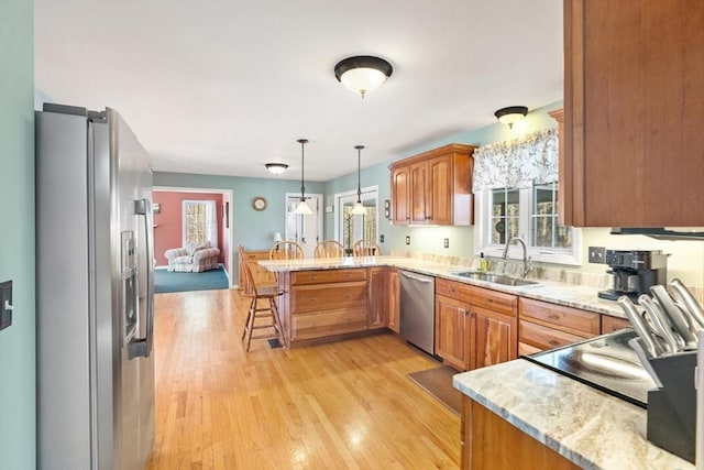 kitchen with kitchen peninsula, pendant lighting, stainless steel appliances, a kitchen bar, and sink