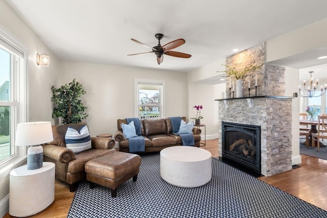living area featuring wood finished floors, ceiling fan, a fireplace, and a chandelier