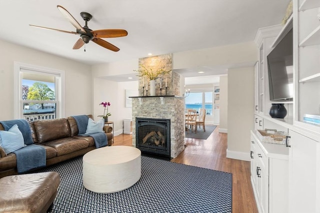 living room featuring wood finished floors, ceiling fan, baseboards, a fireplace, and recessed lighting