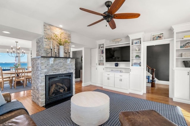 living area with light wood-style flooring, a ceiling fan, and a stone fireplace