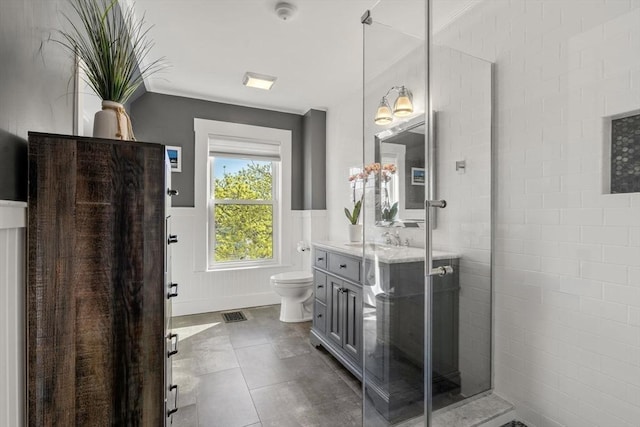 bathroom with vanity, a wainscoted wall, toilet, a tile shower, and tile patterned floors