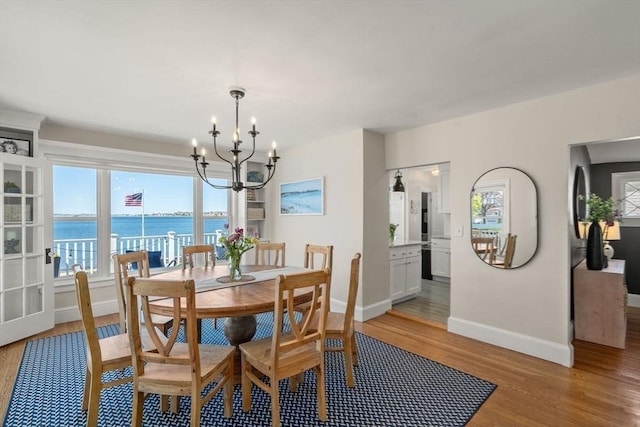 dining room with a chandelier, baseboards, light wood-style flooring, and a water view