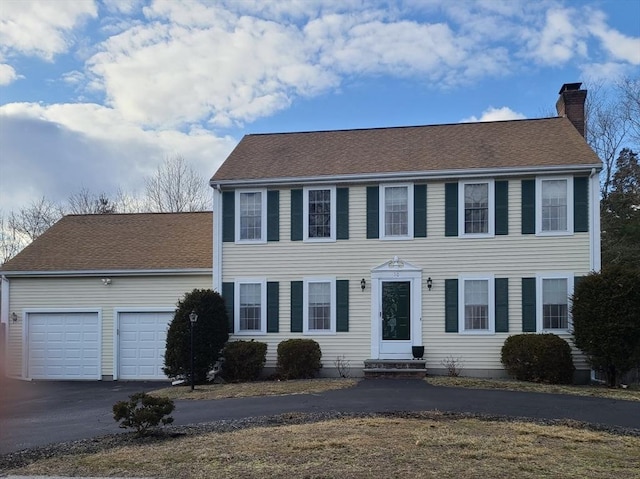 colonial home with driveway, entry steps, an attached garage, a shingled roof, and a chimney