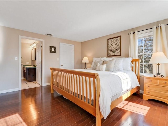 bedroom with wood finished floors, visible vents, ensuite bathroom, and baseboards