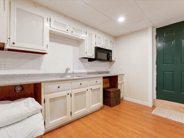 kitchen featuring light wood-style flooring, a sink, white cabinets, black microwave, and light countertops