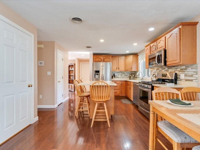 kitchen featuring stainless steel appliances, a kitchen bar, light countertops, and dark wood-style flooring