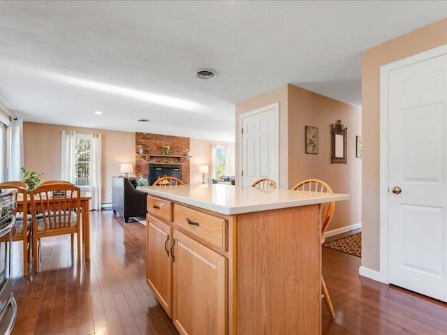 kitchen featuring visible vents, a brick fireplace, dark wood-type flooring, a breakfast bar, and light countertops