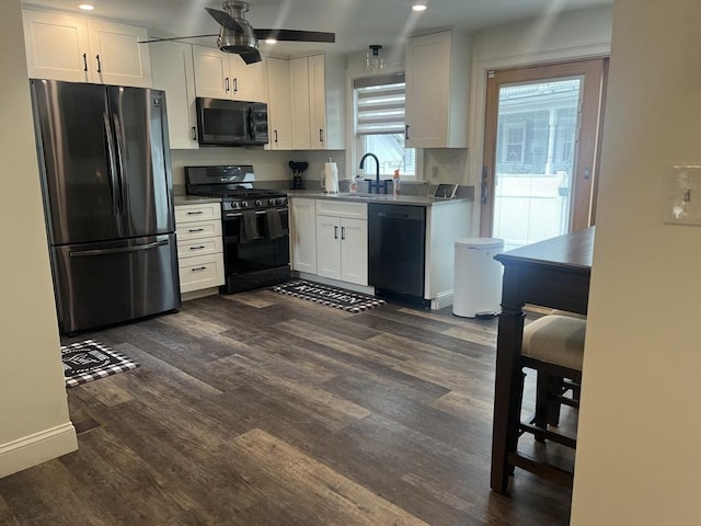 kitchen featuring dark wood finished floors, white cabinets, black appliances, ceiling fan, and a sink