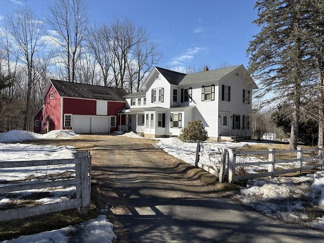 colonial house featuring driveway, a fenced front yard, an outdoor structure, a garage, and a chimney