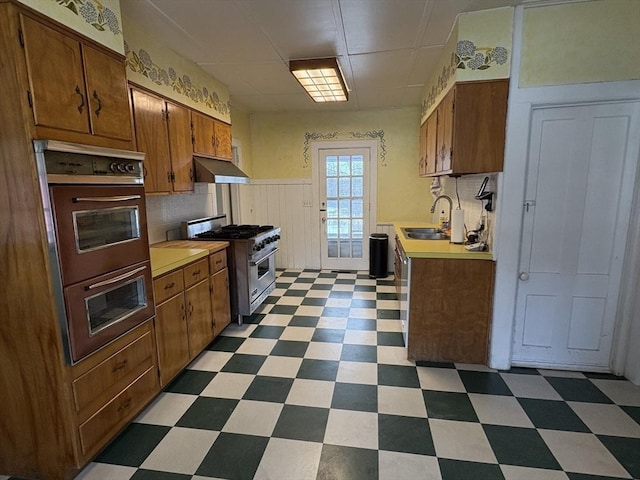 kitchen with a sink, light countertops, under cabinet range hood, high end stainless steel range oven, and tile patterned floors