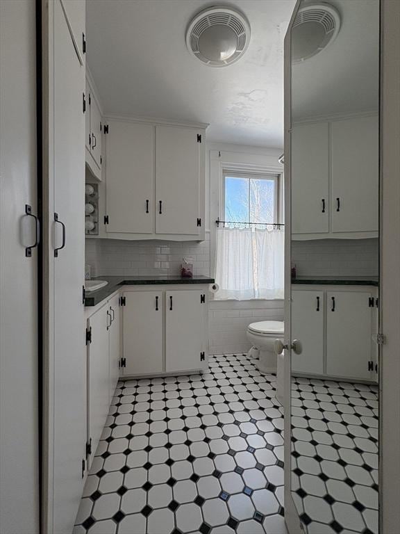 kitchen featuring light floors, visible vents, decorative backsplash, white cabinetry, and dark countertops