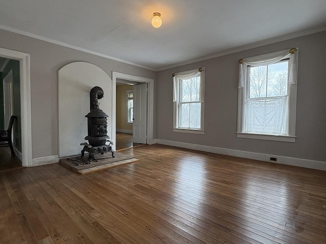 unfurnished living room with hardwood / wood-style flooring, a wood stove, baseboards, and ornamental molding