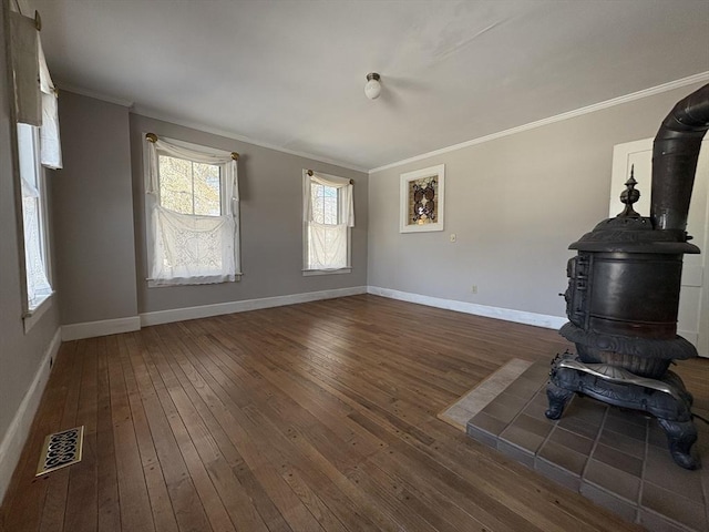 unfurnished living room featuring hardwood / wood-style floors, baseboards, visible vents, a wood stove, and crown molding