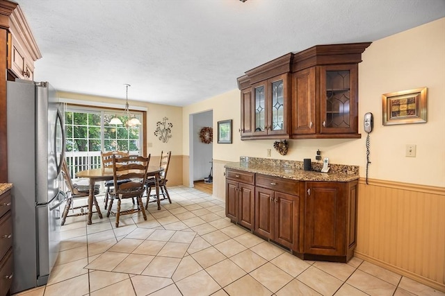 19 K St, Weymouth, MA 02189 - kitchen featuring freestanding refrigerator, light tile patterned floors, light stone counters, wainscoting, and glass insert cabinets