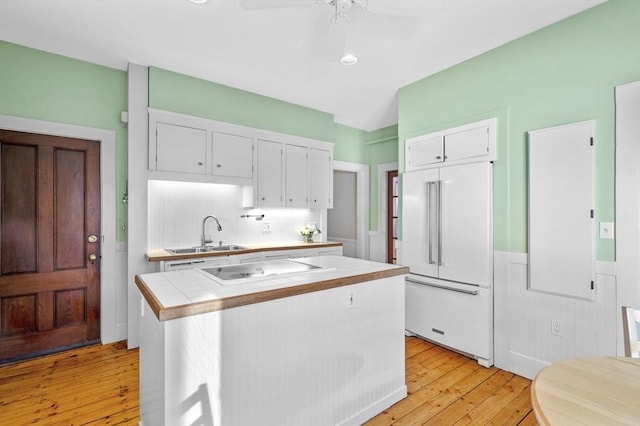 kitchen featuring sink, cooktop, built in refrigerator, light hardwood / wood-style floors, and white cabinets